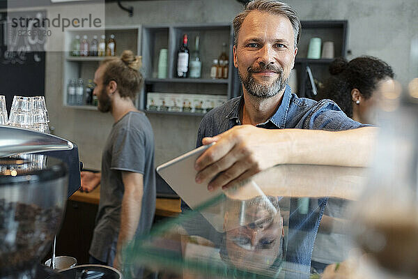Lächelnder Coffeeshop-Besitzer steht hinter dem Schrank im Café