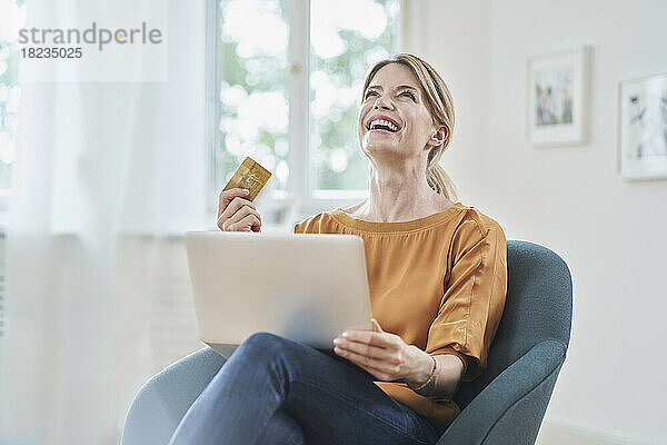 Glückliche Frau mit Kreditkarte genießt Online-Shopping per Laptop zu Hause