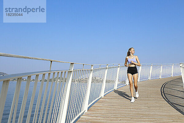 Glückliche junge Frau joggt auf erhöhtem Gehweg