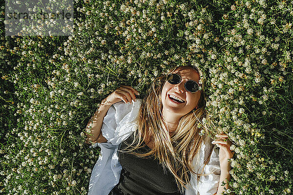 Glückliche Frau mit Sonnenbrille liegt auf einer Wiese voller Kleeblumen