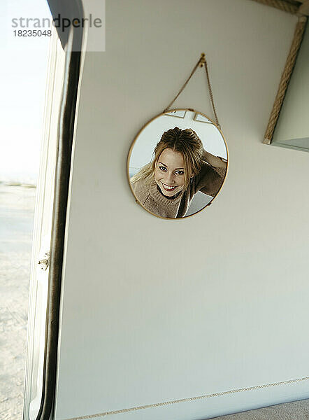 Smiling woman's reflection in mirror hanging in caravan