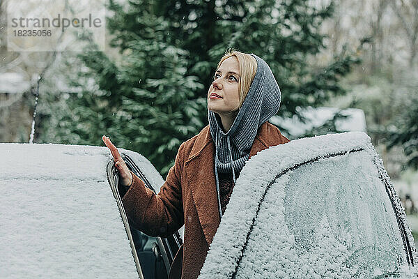 Nachdenkliche Frau am Auto im Winter mit Schnee bedeckt