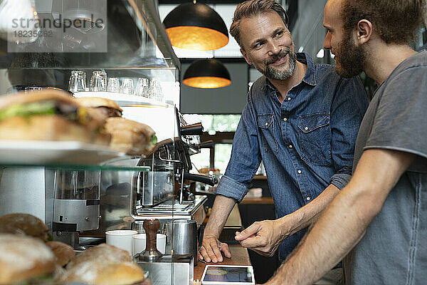 Lächelnder Cafébesitzer im Gespräch mit Barista im Café