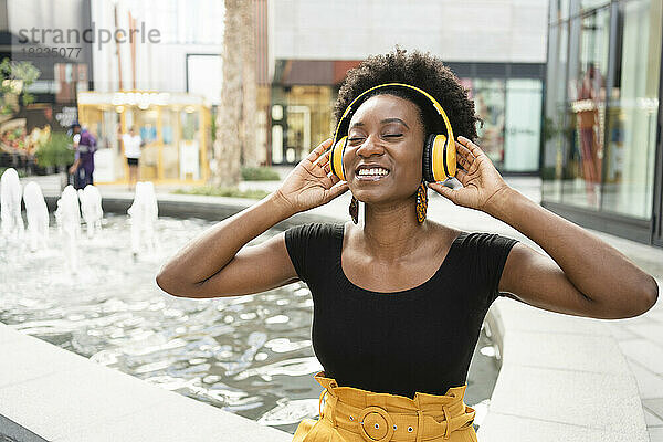 Glückliche Frau mit Kopfhörern  die an der Wand Musik hört