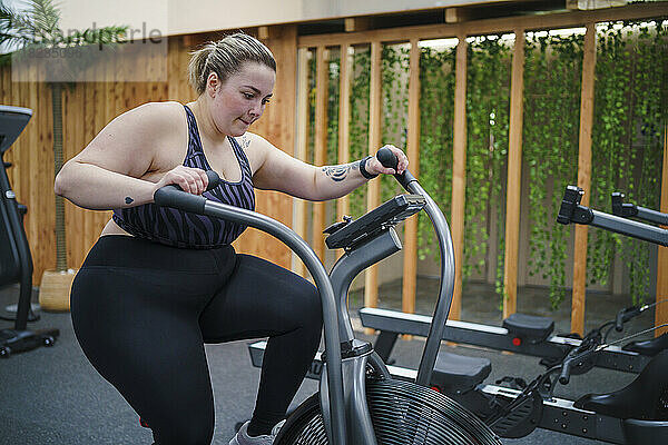 Übergewichtige Frau trainiert im Fitnessstudio auf dem Crosstrainer