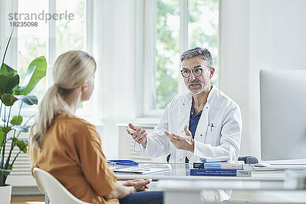 Arzt bespricht sich mit Patient  der am Schreibtisch in der Arztpraxis sitzt