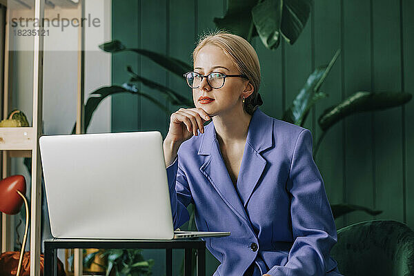 Nachdenkliche Geschäftsfrau mit Laptop sitzt im Heimbüro