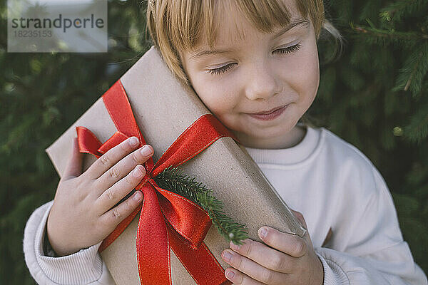 Mädchen mit geschlossenen Augen hält Weihnachtsgeschenkbox