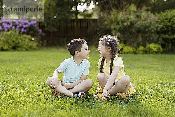 Glücklicher Bruder und Schwester sitzen auf Gras im Garten