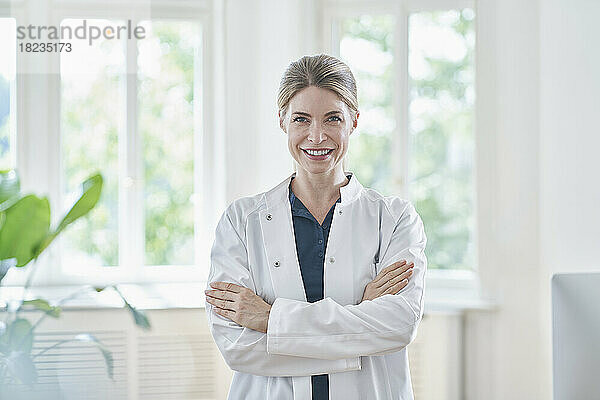 Happy female doctor wearing lab coat standing at medical practice