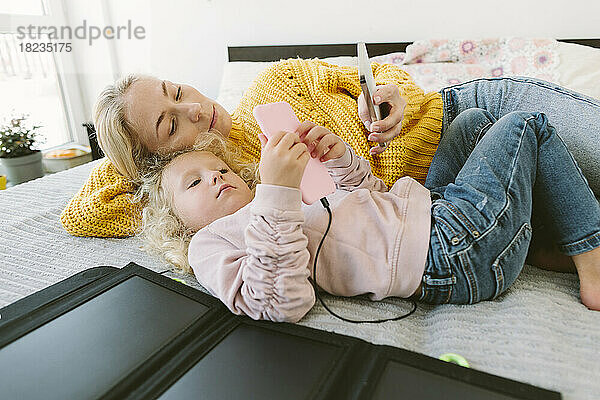 Mutter und Tochter benutzen Mobiltelefone  die zu Hause im Bett liegen