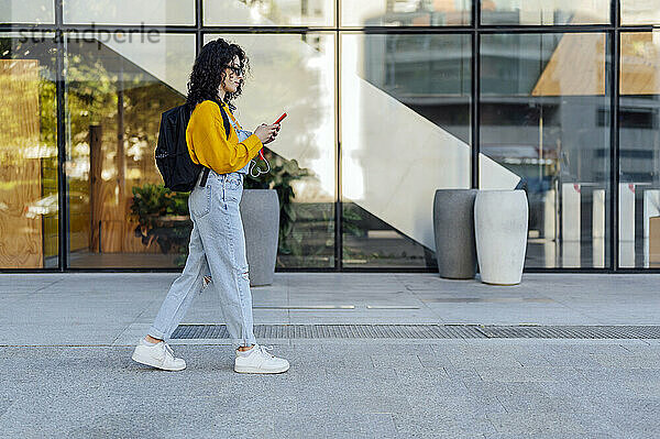 Junge Frau mit Rucksack benutzt Smartphone auf Fußweg