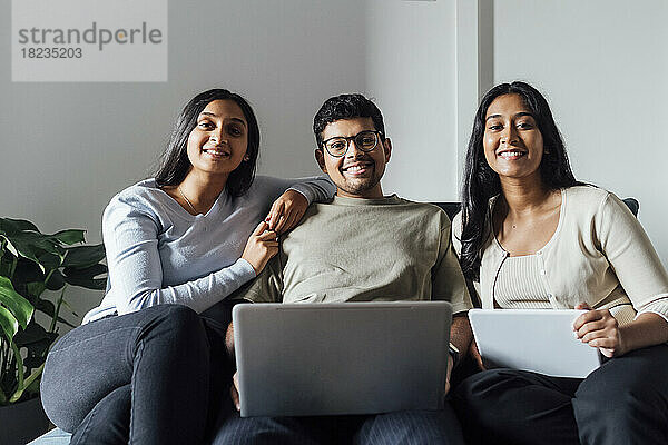 Lächelnde Frauen und Männer mit Laptop und digitalem Tablet sitzen auf dem Sofa