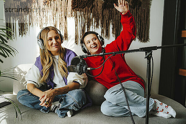 Glücklicher Musiker mit Kollege  der Kopfhörer vor dem Mikrofon im Studio trägt