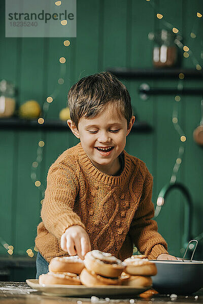 Fröhlicher Junge mit Zimtschnecken in der Küche