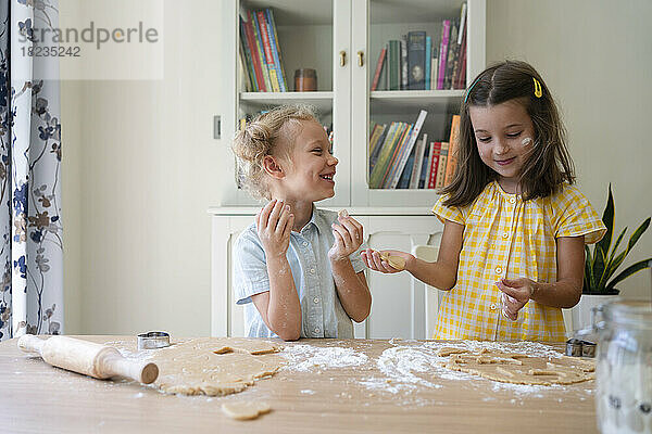 Happy cute girls preparing cookies with dough on table at home