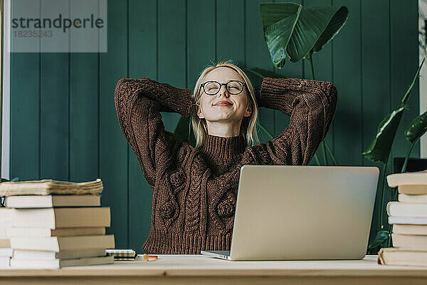 Geschäftsfrau mit den Händen hinter dem Kopf entspannt sich im Heimbüro