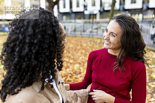 Lächelnde Frau blickt Freundin im Herbstpark an