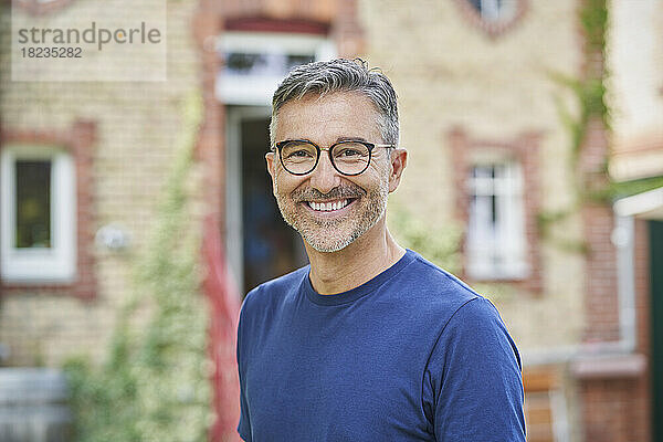 Lächelnder Mann mit Brille vor dem Haus