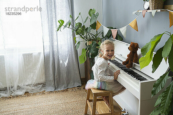 Glückliches Mädchen  das zu Hause auf einem Hocker am Klavier sitzt