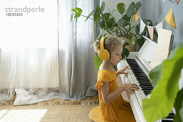 Mädchen mit Kopfhörern spielt zu Hause Klavier