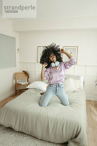 Glückliche Frau mit kabellosen Kopfhörern  die zu Hause auf dem Bett tanzt
