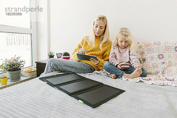 Mutter benutzt Tablet-PC mit Solarbatterieladegerät auf dem Bett im Schlafzimmer