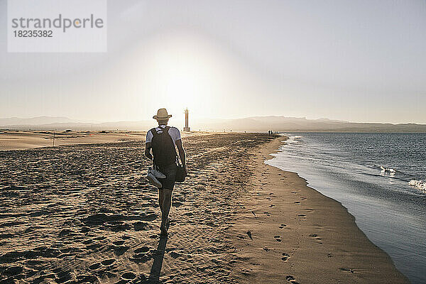 Mann geht bei Sonnenuntergang in Ufernähe am Strand spazieren