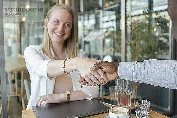 Glückliche Geschäftsfrau schüttelt einem Kollegen im Café die Hand