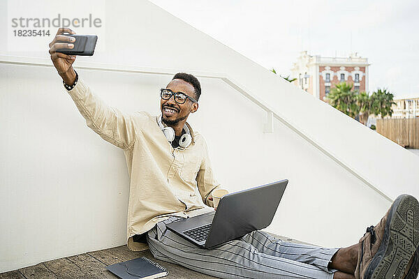 Glücklicher Freiberufler  der mit dem Laptop ein Selfie per Smartphone macht
