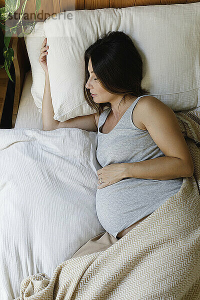 Pregnant mature woman sleeping on bed at home
