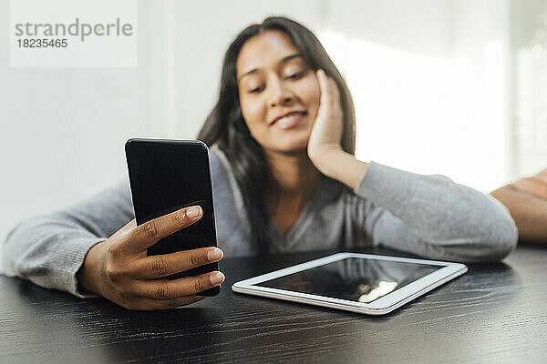 Lächelnde Frau mit Smartphone und Tablet-PC auf dem heimischen Tisch