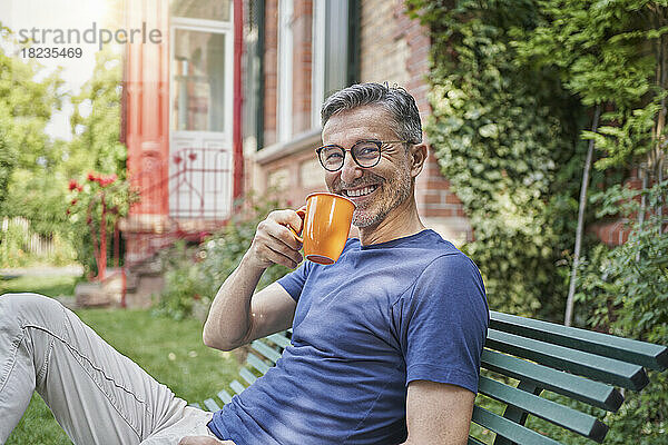 Glücklicher Mann hält Kaffeetasse auf Bank im Garten