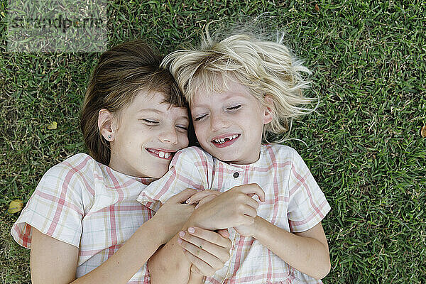 Lächelndes Mädchen mit Schwester  die auf Gras liegt