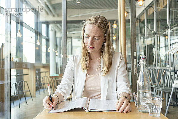 Junge Geschäftsfrau markiert im Café Zeitschrift mit Stift