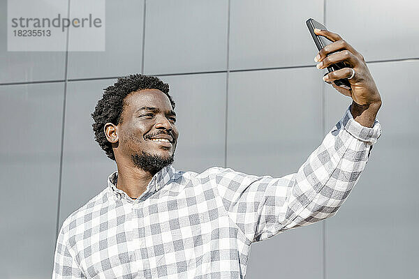 Mann macht Selfie mit Smartphone vor Wand