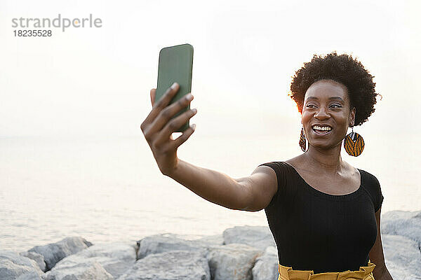 Glückliche Frau  die bei Sonnenuntergang ein Selfie mit dem Handy macht