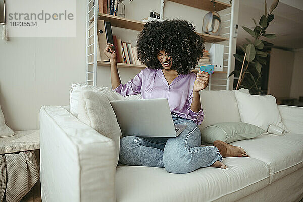 Glückliche Frau mit Kreditkarte beim Online-Shopping am Laptop zu Hause