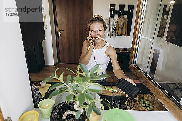 Glückliche Frau am Telefon  aufgeladen durch Solarbatterie in der Küche