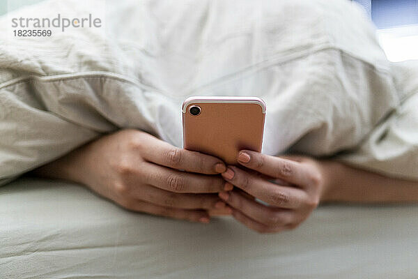 Hände einer Frau  die zu Hause im Bett ihr Smartphone benutzt