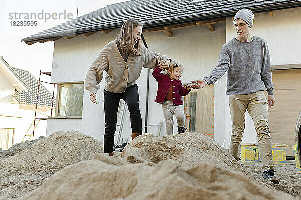 Niedliches kleines Mädchen  das mit den Eltern auf einem Sandhaufen spielt