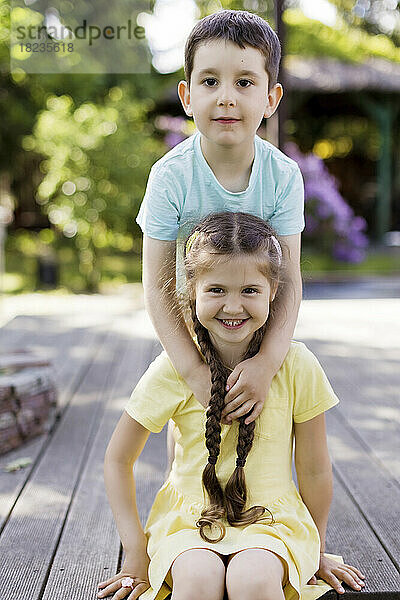 Lächelnder Junge mit Schwester sitzt im Garten