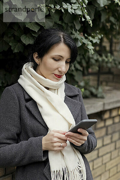 Frau mit Schal und Smartphone bei Pflanzen