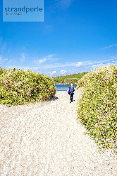 UK  Scotland  Female hiker walking between grassy dunes of Scousburgh Sands