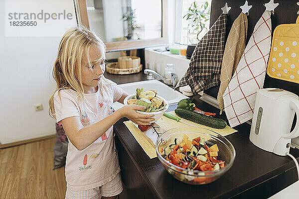 Girl collecting organic waste from vegetables in kitchen