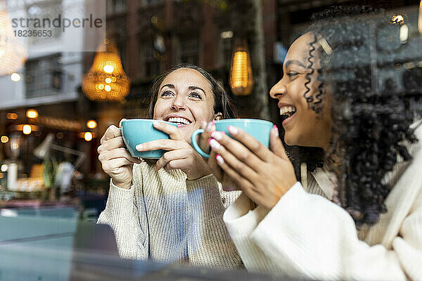 Nachdenkliche Frau beim Kaffeetrinken mit einer Freundin im Café  gesehen durch Glas