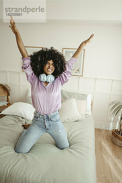 Afro-Frau mit erhobenen Armen tanzt auf dem Bett im Schlafzimmer