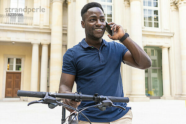 Lächelnder Mann telefoniert und steht mit dem Fahrrad vor dem Gebäude