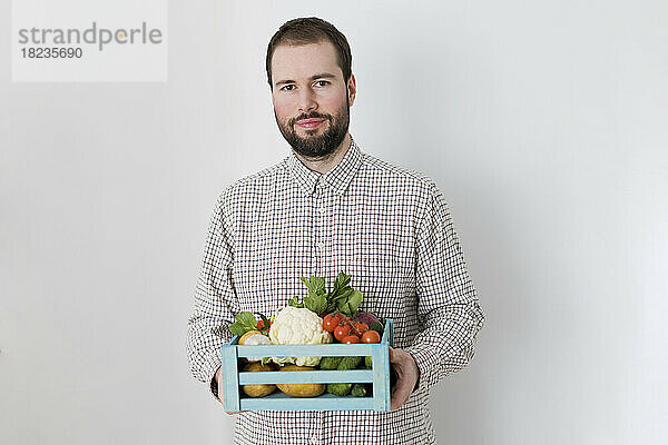 Man holding crate of organic vegetables against white background