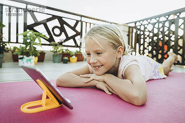 Lächelndes Mädchen  das sich auf der Terrasse entspannt und auf sein Mobiltelefon schaut